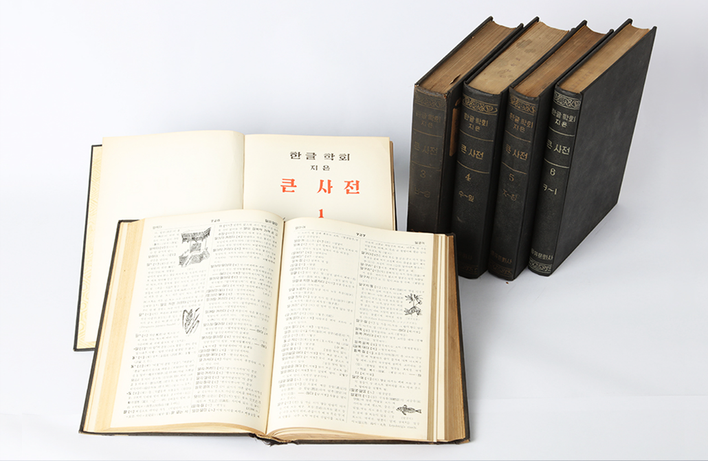 1957년 전체가 완성된 한글학회의 『큰사전』 6권 사진이다. 앞쪽에는 두 권의 큰사전이 펼쳐져 있고, 뒤에는 큰사전 네 권이 세워져 있다. 