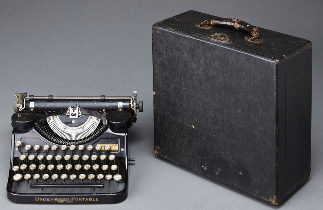 '송기주 네벌식 한글 타자기' 사진이다. 왼쪽에는 검은색 금속 재질의 타자기가 놓여 있으며, 둥근 흰색 키가 여러 줄로 배열되어 있고 각 키에는 글자를 입력할 수 있는 표기가 새겨져 있다. 오른쪽에는 네모난 검은색 가방 케이스가 세워져 있다.