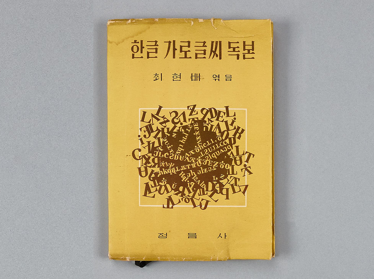 『한글 가로글씨 독본』 초반푠 표지다. 노란색 표지이며, ‘한글 가로글씨 득본’이라는 제목과 함께 저자 이름이 적혀있다. 표지 중앙에는 다양한 알파벳 글자가 뒤섞여 있는 그래픽 이미지가 있다.