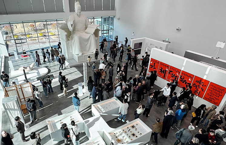 김해 순회전 및 세종대왕 동상 원형 사진이다. 김해 순회전 전시 현장을 위에서 내려다본 찍은 사진으로, 중앙에는 많은 관람객들이 모여 전시 작품을 둘러보고 있다. 세종대왕 동상 원형에서 세종대왕은 한 손을 들어 올리고 있고, 다른 손에는 훈민정음 해례본을 들고 있다.