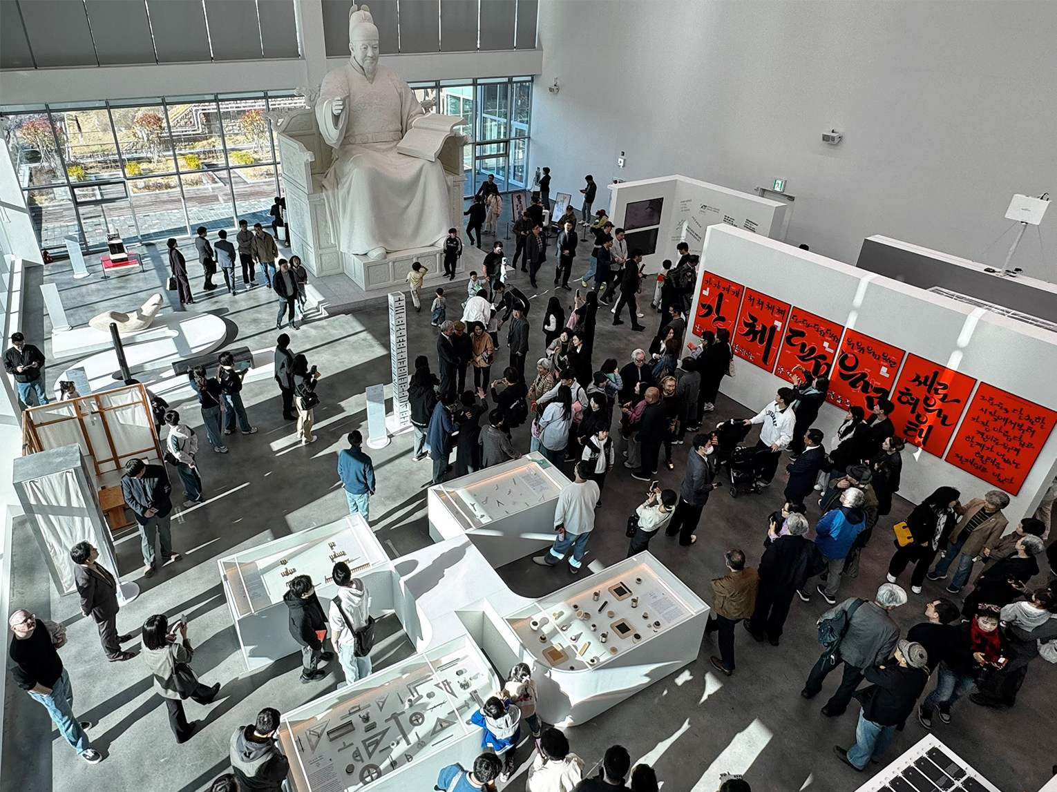 김해 순회전 및 세종대왕 동상 원형 사진이다. 김해 순회전 전시 현장을 위에서 내려다본 찍은 사진으로, 중앙에는 많은 관람객들이 모여 전시 작품을 둘러보고 있다. 세종대왕 동상 원형에서 세종대왕은 한 손을 들어 올리고 있고, 다른 손에는 훈민정음 해례본을 들고 있다.