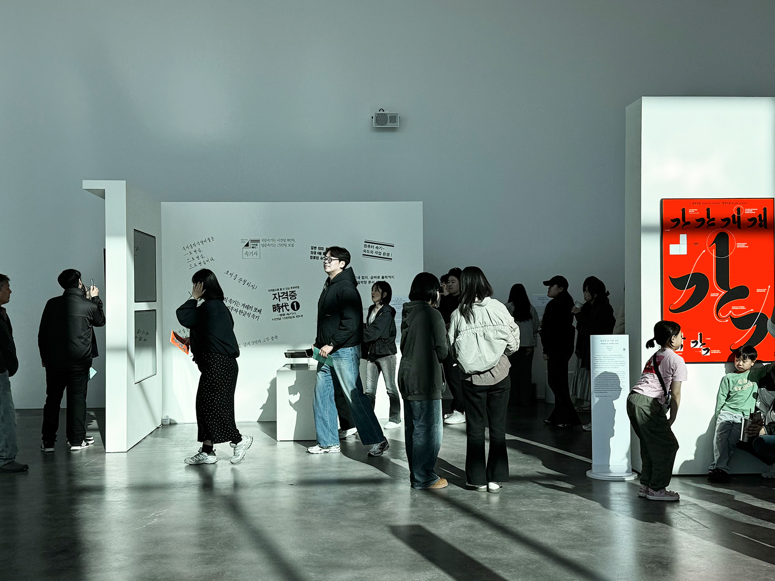 <글(자)감(각): 쓰기와 도구> 김해 순회전 현장 사진이다. 흰 벽 전시 공간에서 사람들이 작품 앞에 줄지어 서서 관람하고 있다.