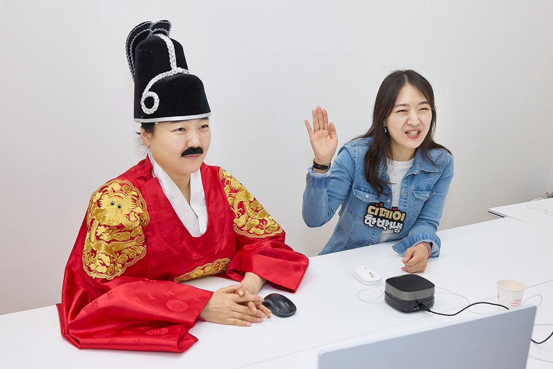 ｢한글이 보이는 라디오｣ 원격 교육 화면이다. 한 인물은 곤룡포를 입고 왕의 모습을 하고 있으며, 그 옆에 진행자는 손을 들며 밝게 웃고 있다.