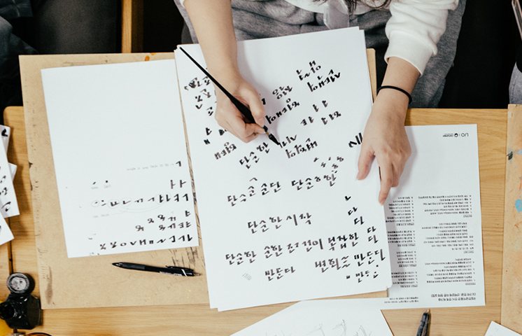  ‘인벤타리오 문구 박람회’ 워크숍 ‘보이지 않아도 알 수 있는 또 하나의 한글’ 사진이다. 한 사람이 붓펜을 들고 흰 종이에 한글 글자를 써 내려가고 있다.