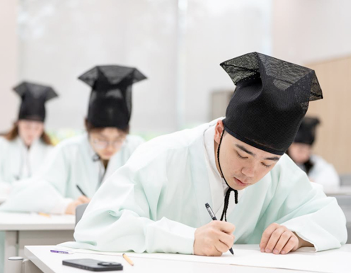 ‘2025 세종학당 한국어 말하기·쓰기 대회 결선 현장’ 사진이다. 전통 유생 복장을 한 참가자가 책상에 앉아 진지한 표정으로 글을 쓰고 있다.