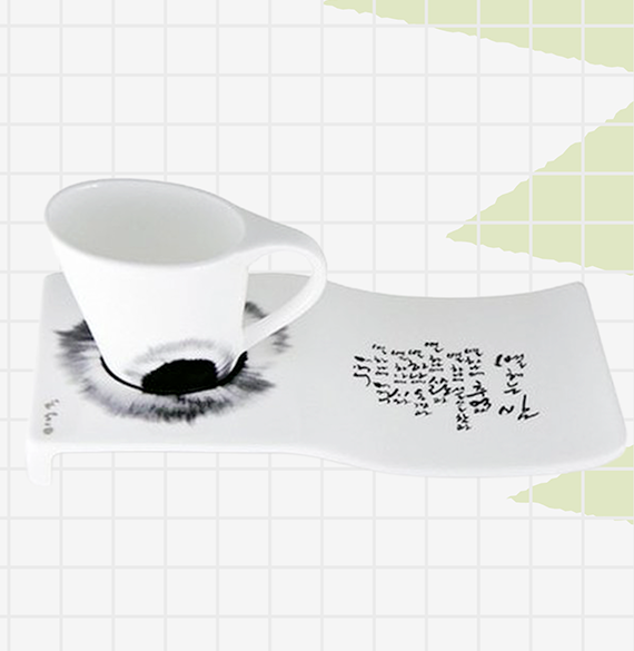 흰색 커피잔과 받침 위에 먹 번짐 효과와 한글 캘리그래피가 장식되어 있다.