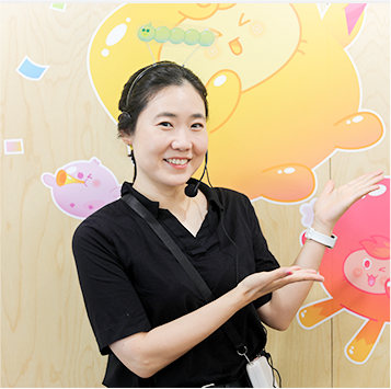 검은색 블라우스를 입고 마이크를 찬 방소정 교육 강사가 손으로 말랑통통 캐릭터를 가리키고 있다.