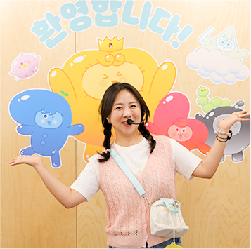 마이크를 찬 김지은 교육 강사가 말랑통통 캐릭터가 그려진 벽 앞에서 환하게 웃고 있다.