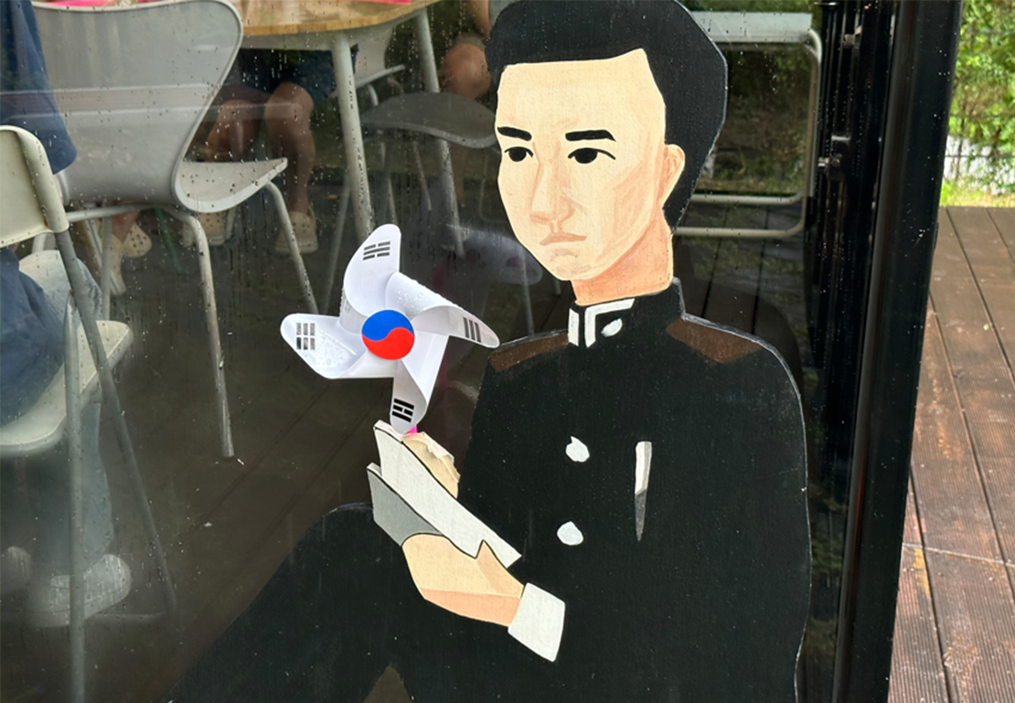 책을 든 윤동주 인물 조형물 옆에 태극 문양 바람개비가 설치되어 있다.