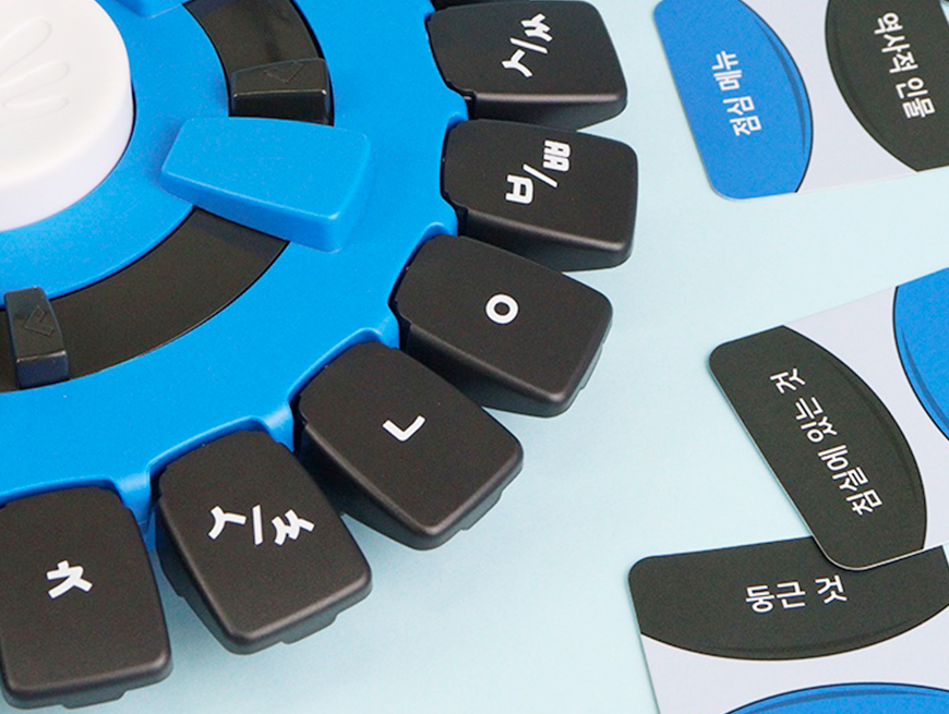 파란색 원형 장치 주변에 한글 자모 타일과 ‘한글 모음’, ‘예외모음’, ‘둥근 것’ 등의 단어 카드가 배치되어 있다.