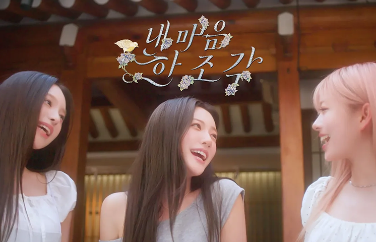 앳하트의 ‘내 마음 한 조각’ 뮤직비디오 미리보기 이미지로, 앳하트 멤버 세 명이 서로를 바라보며 웃고 있다. 상단에는 ‘내 마음 한 조각’ 노래 제목이 손 글씨 형태로 표현되어 있다.