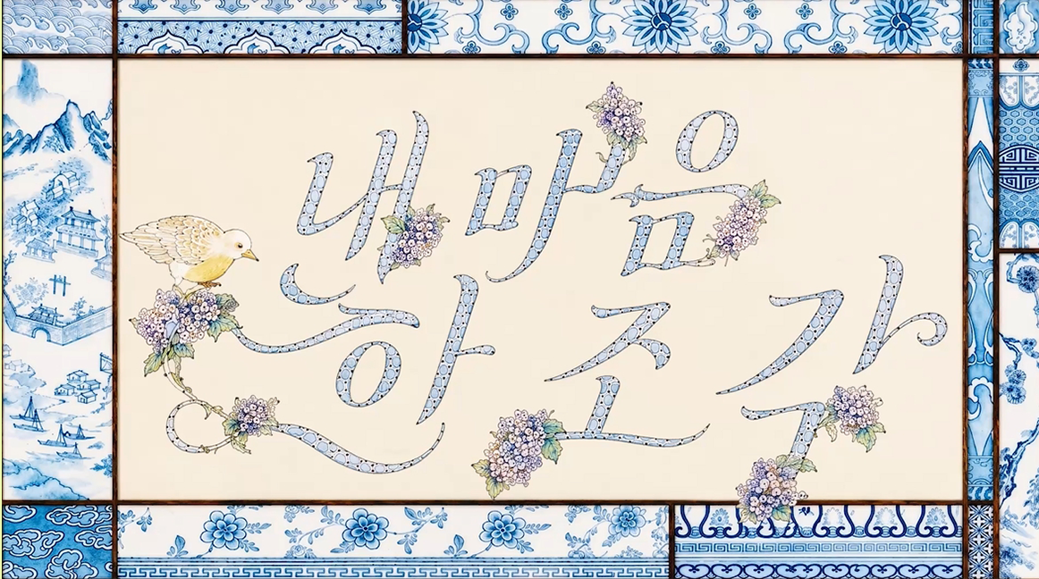 앳하트의 ‘내 마음 한 조각’ 뮤직비디오 속 장면으로, 푸른색 꽃무늬 장식 테두리 안에 꽃과 작은 새가 어우러져 있으며 중앙에는 ‘내 마음 한 조각’이라는 문구가 손 글씨 형태로 표현되어 있다.