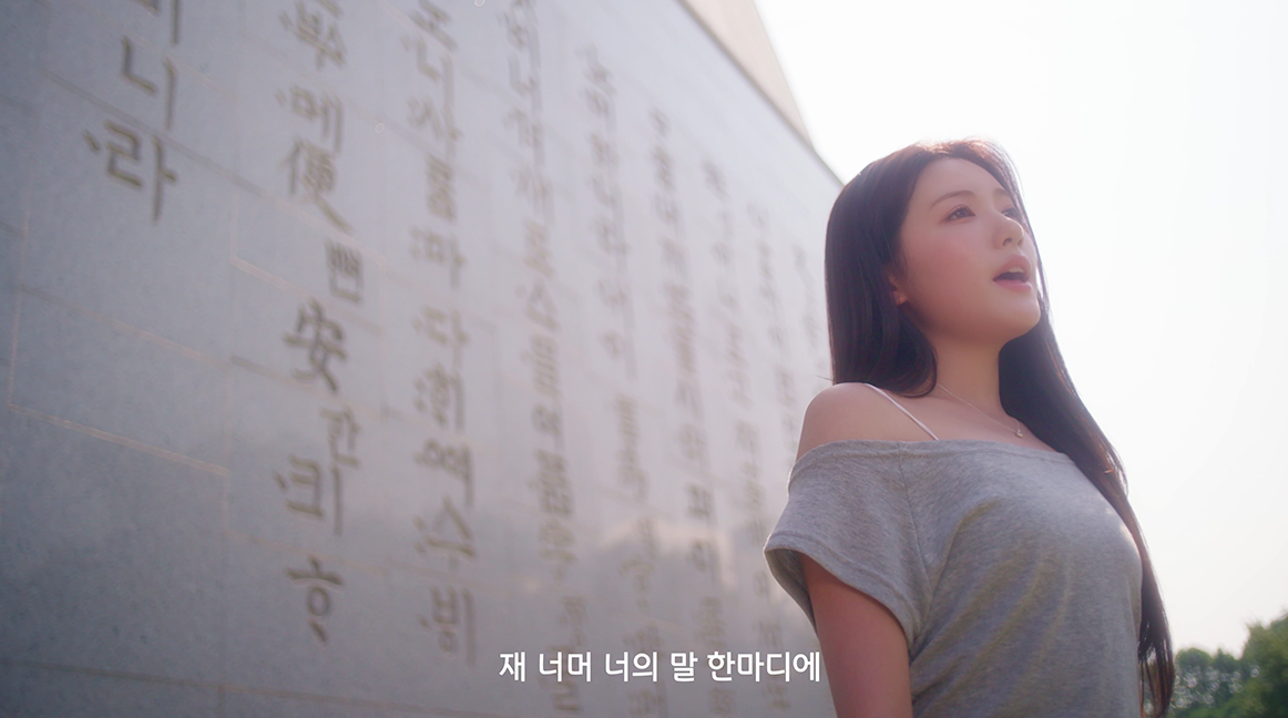 앳하트의 ‘내 마음 한 조각’ 뮤직비디오 속 장면으로, 훈민정음이 쓰인 벽 앞에서 멤버 서현이 노래를 부르고 있다.