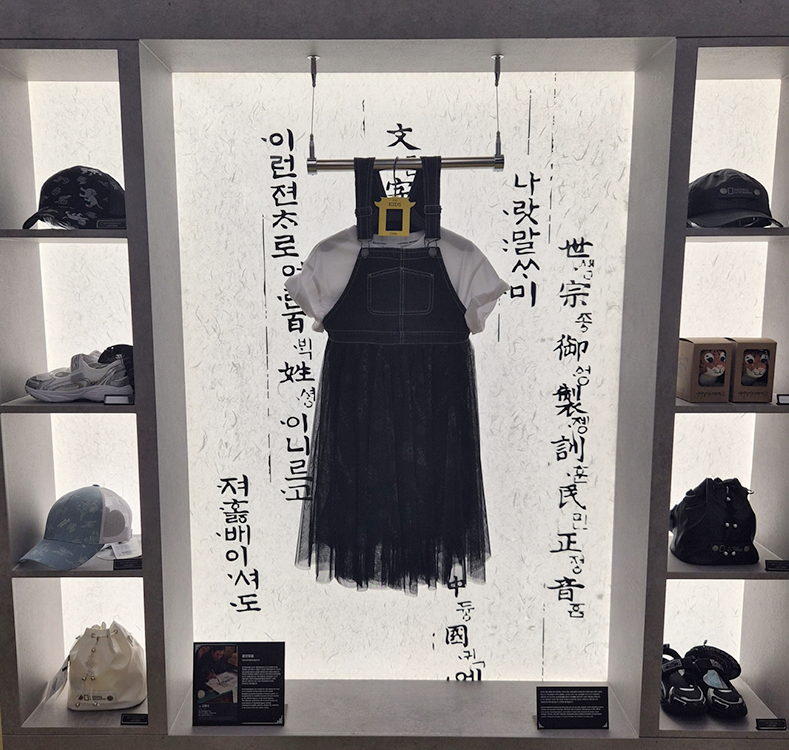 내셔널지오그래픽 어패럴이 국가유산청과 협업한 선보인 ‘K-헤리티지’ 반짝매장 모습이다. 중앙에 훈민정음이 쓰인 벽이 있고, 그 앞에 의상이 전시되어 있다. 주변에는 모자와 신발, 가방 등의 관련 상품이 함께 배치되어 있다.